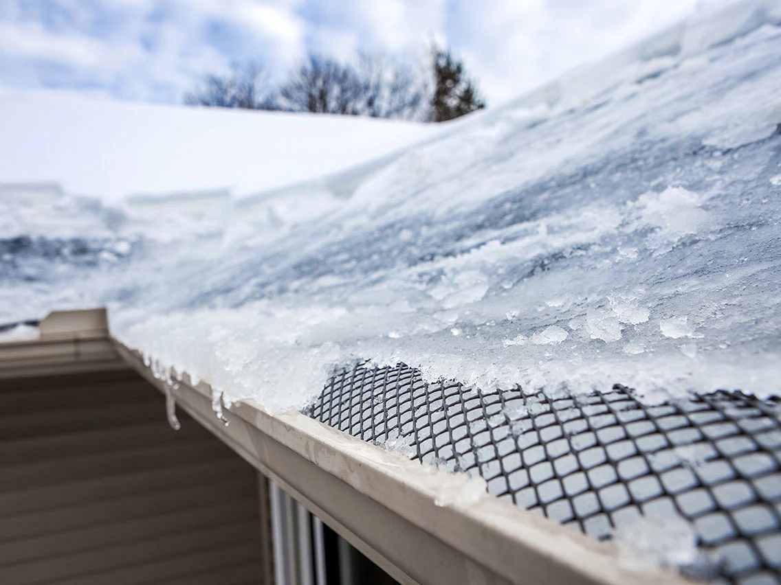 Ice dams forming on a roof with gutter guard protection, showing winter gutter maintenance importance for safety.