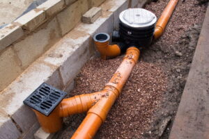 Efficient underground drainage system installation featuring orange pipes and a drainage grate, ensuring proper water management and preventing foundation damage.