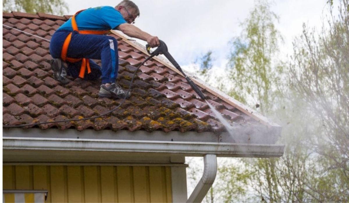 a man on top of the roof pressure washing the roof and gutters
