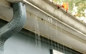 Overflowing gutter with visible water damage and a blocked leaf, illustrating the need for gutter repair.