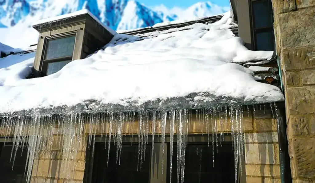 Roof covered in snow with icicles and ice dams causing potential winter damage to the structure.