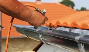 A professional repairing a roof gutter using specialized tools to ensure proper function.