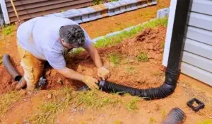 Technician repairing an underground gutter drain connected to a downspout at a suburban Chicagoland home.