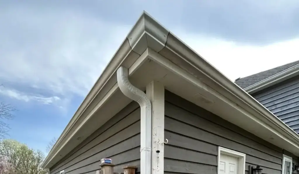 Seamless gutters installed along the roofline of a gray suburban home with corner downspout and siding detail.