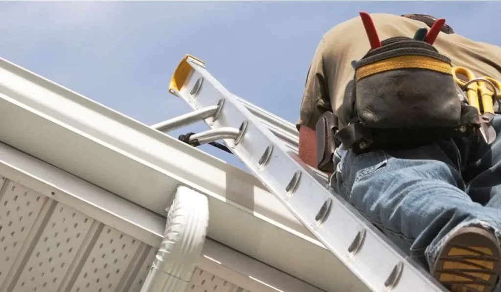 Worker on ladder performing gutter replacement with seamless system to improve drainage and prevent water damage.