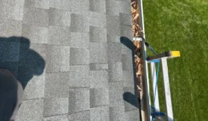 Clogged gutter filled with leaves beside a residential roof, highlighting the need for professional Roof and Gutter Cleaning to prevent water damage and overflow.