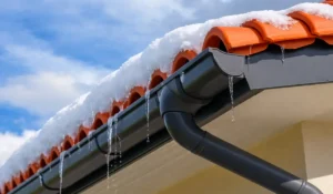 Melting snow and icicles on a roof gutter and downspout system showing why homeowners should inspect your downspout before spring thaw to prevent water overflow and foundation damage.