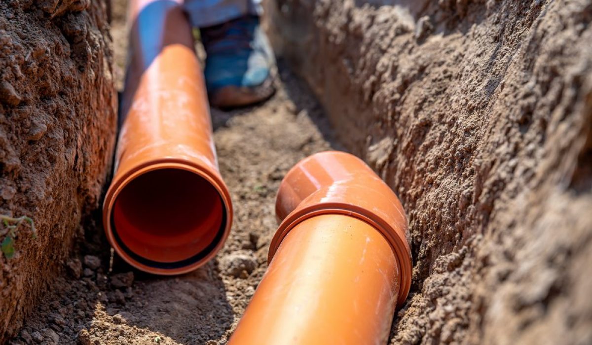 Close-up of an orange underground drainage system being installed in a trench, highlighting the pipes and the surrounding soil.